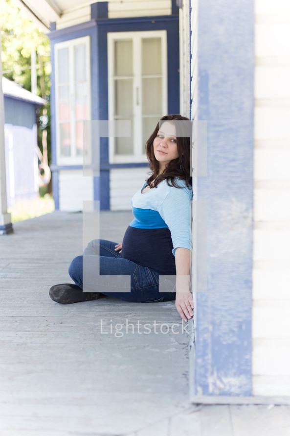 Pregnant woman sitting on the ground leaning against a house.