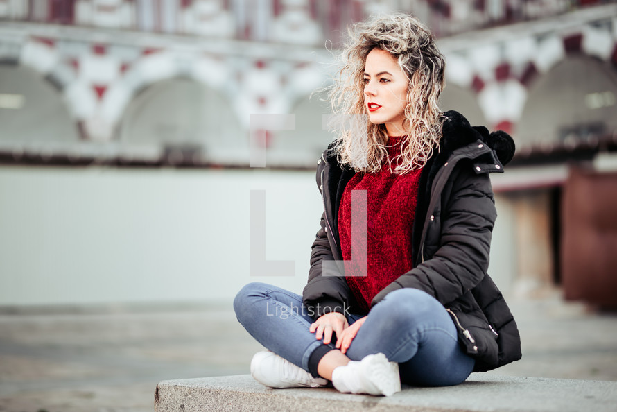 curly haired blonde woman sitting on beach. Casual clothes