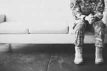 Female soldier in uniform sitting on a sofa praying.
