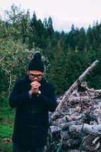a man praying outdoors with a pile of firewood 