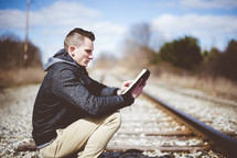 man reading a Bible on train tracks 