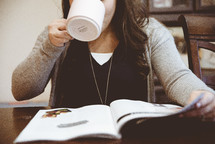 a woman reading a magazine and drinking coffee 