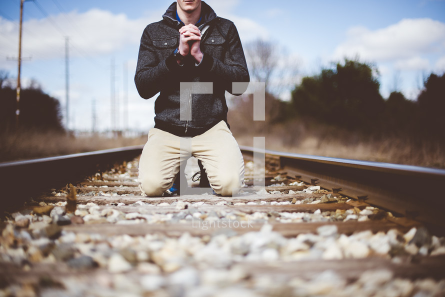 a man kneeling in prayer in the middle of train tracks 
