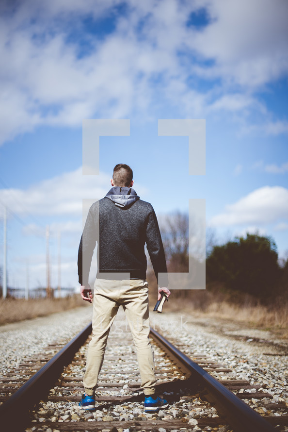 man standing holding a Bible in the middle of train tracks 