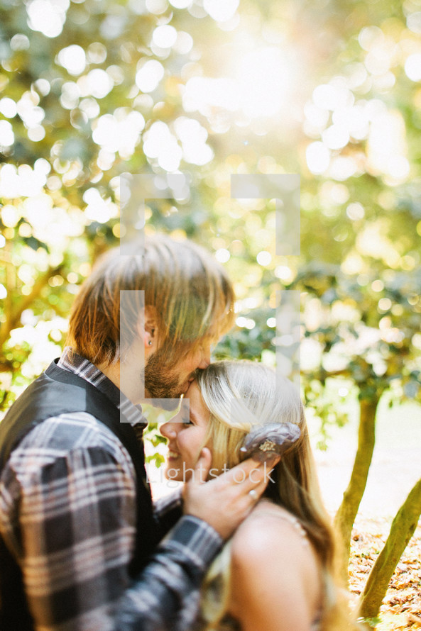 Man facing woman kissing her forehead with trees in background.