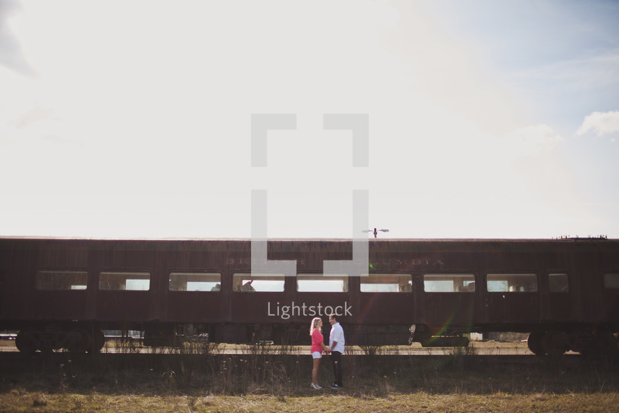 man and woman holding hands standing in front of an old railway car