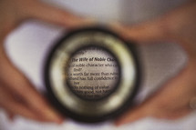 Hands holding magnifying glass over "The Wife of Noble Character" scripture.