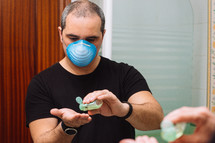 man with face mask applying disinfectant sanitizer onto hand for protection against virus germs
