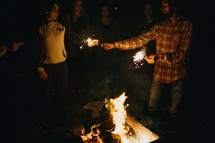 people lighting sparklers around a campfire 