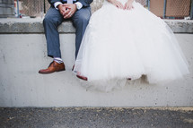 legs of a bride and groom dangling while sitting on a concrete wall