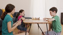 Three kids playing a card game in the living room, shouting and arguing