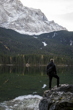 a man standing on a rock by a mountain lake 
