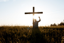 a man standing in a field next to a cross with hand raised 