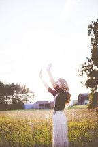 a woman standing outdoors with hands raised praising God 