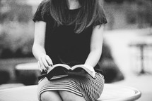 young woman sitting outdoors reading a Bible 