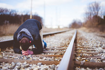 a man kneeling in the middle of train tracks praying 