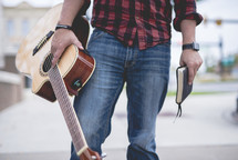 man standing holding a guitar and Bible 