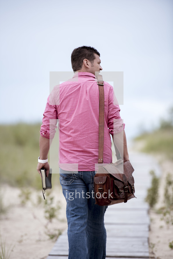 man walking on a boardwalk carrying a Bible 