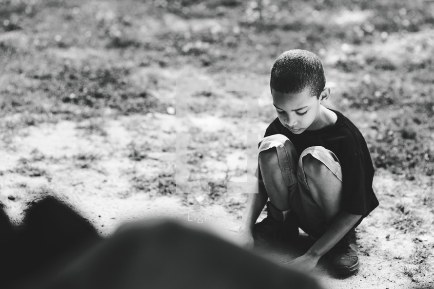 a squatting boy playing in dirt 