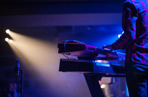 A musician playing a keyboard lit by stage lights.