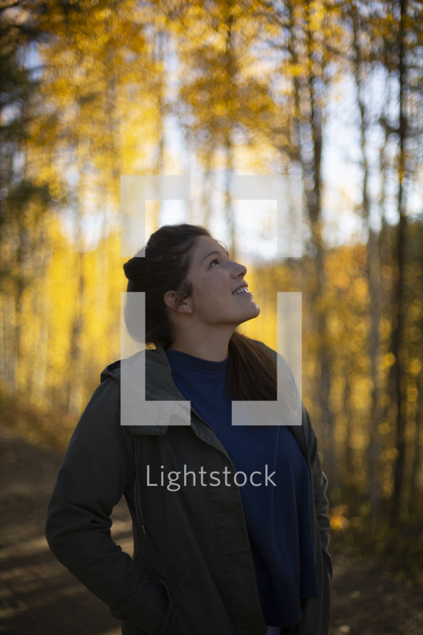 a young woman looking up at fall foliage 