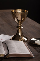 A golden communion goblet, communion wafer and an open Bible.