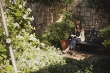 Woman sitting on bench in garden reading the bible.
