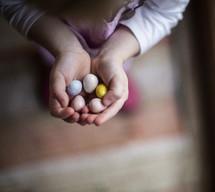 a child with cupped hands holding candy Easter eggs