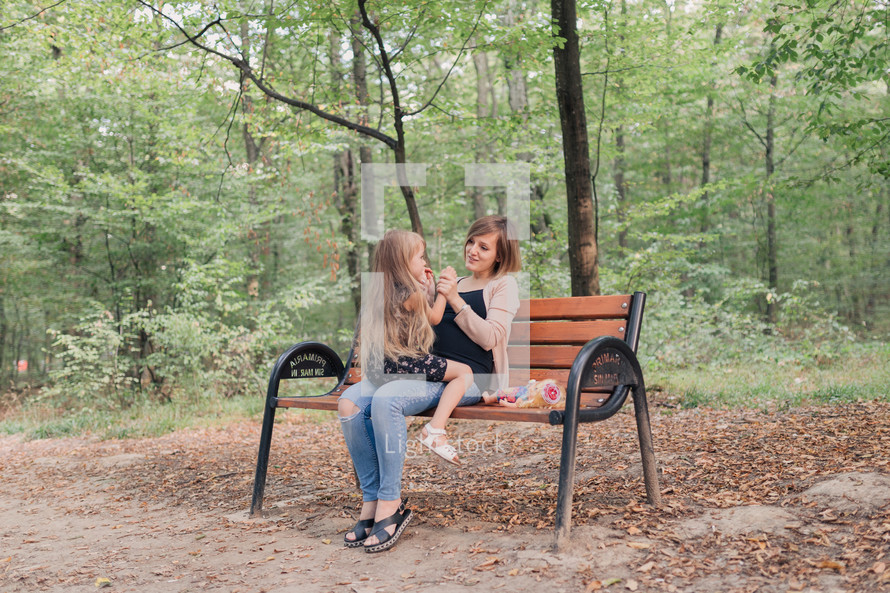 mother and daughter sitting on a park bench 