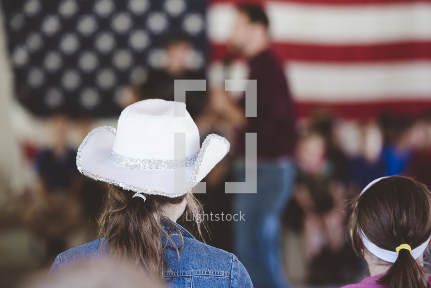 girl in a cowboy hat watching a speaker on stage 