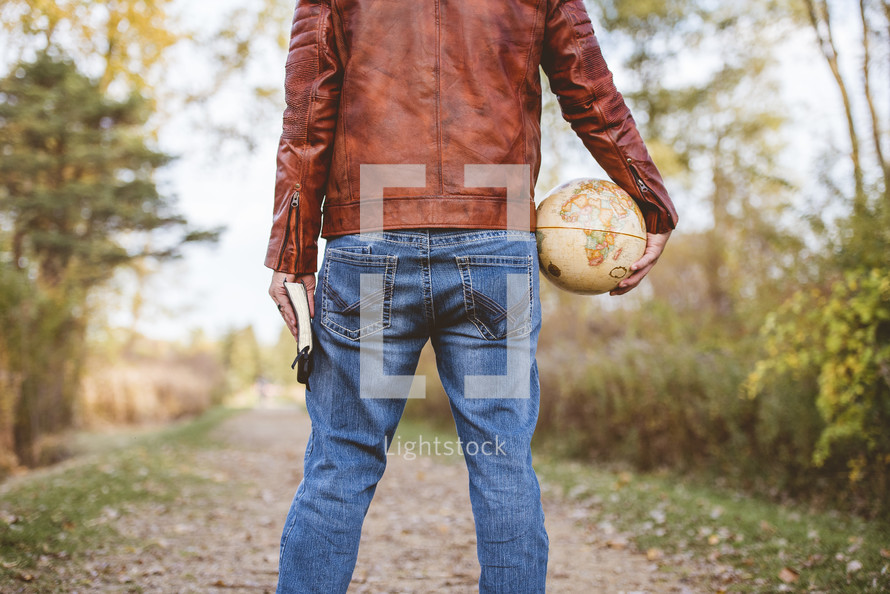 man holding a globe and Bible outdoors 