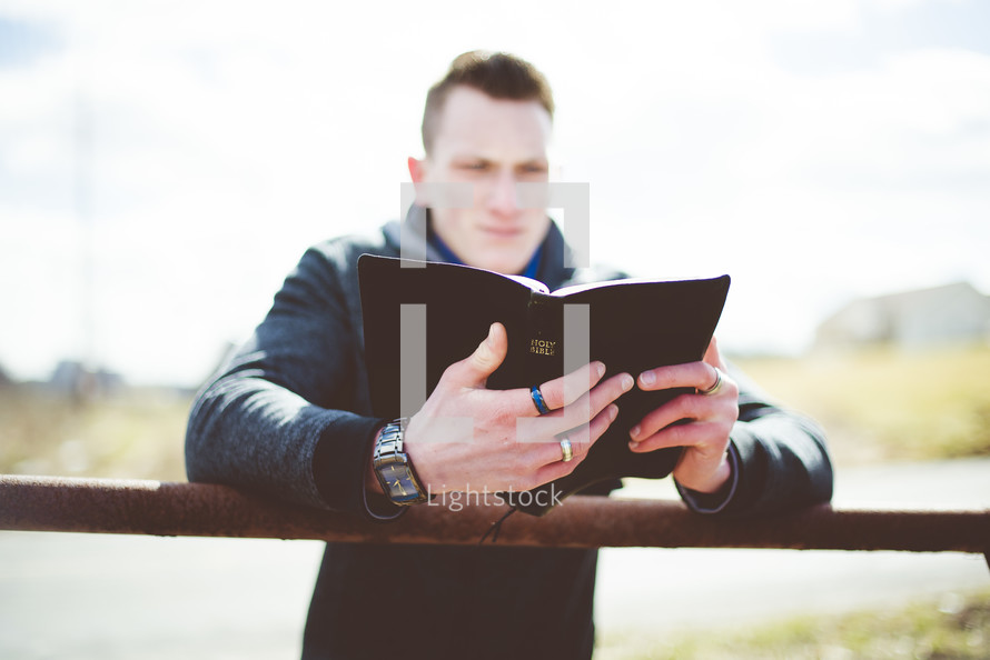 a man reading a Bible leaning over a fence 