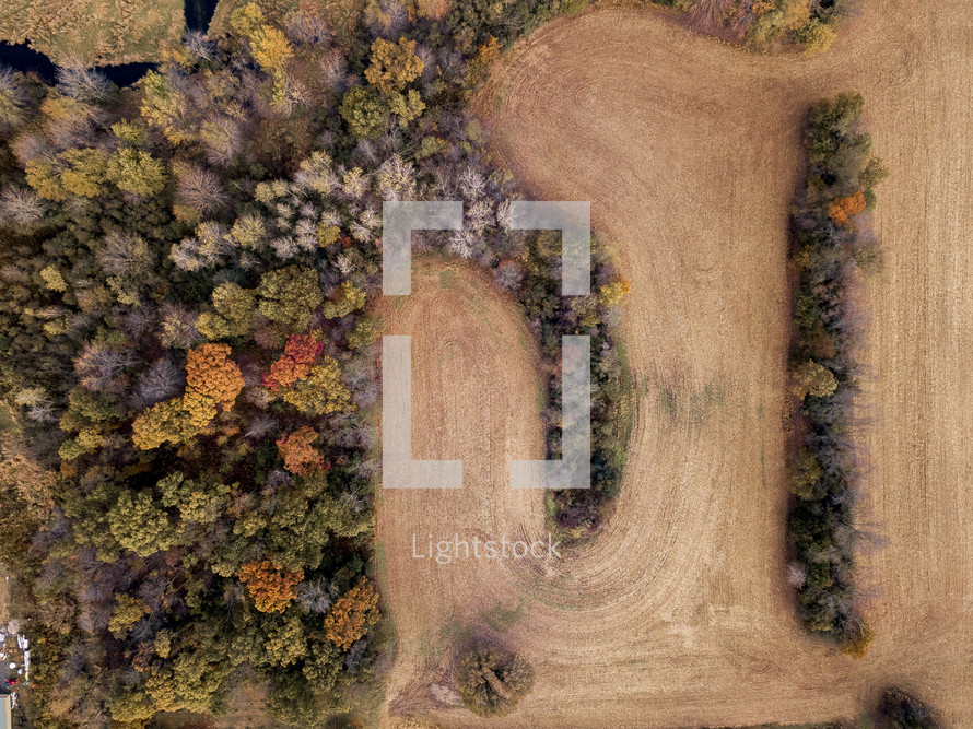 aerial view over a fall forest and plowed field 