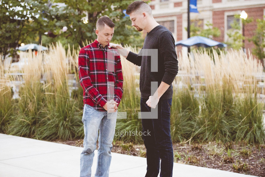 two men praying together outdoors 