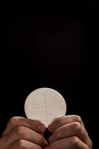 Hands holding a single communion wafer.