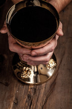 Hands grasping a golden goblet of communion wine.