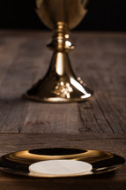 A communion wafer and golden communion goblet on a rustic wooden table.