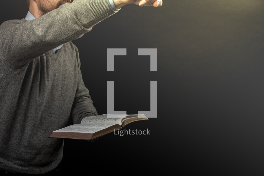 A man pointing and preaching while holding an open Bible.
