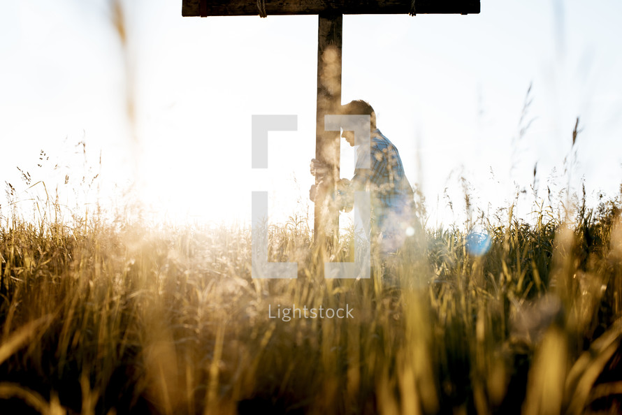 a man standing in a field next to a cross praying 