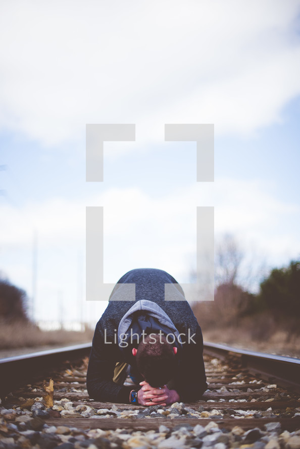 a man kneeling in the middle of train tracks praying 
