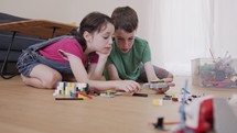 Girl and a boy playing and constructing with toy bricks on the living room floor