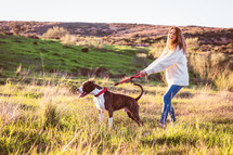 Young woman with white jerser and jeans training American Staffordshire terrier in the field