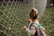 little girl looking through a chain link fence 