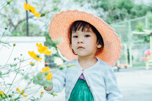 a little girl in a straw hat standing next to flower 