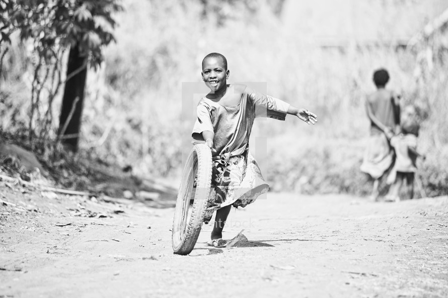A young boy running and playing with a tire.