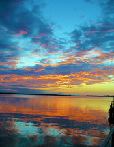 A winter time sunset over a calm peaceful lake with blue, gold and orange colors reflecting from the sunlight in the mirror like reflection of the water.  In the fall and winter seasons we get some of the most amazing sunsets that look like something out of a movie. This image was taken in December one year overlooking Lake Dora in Mount Dora, Florida. 