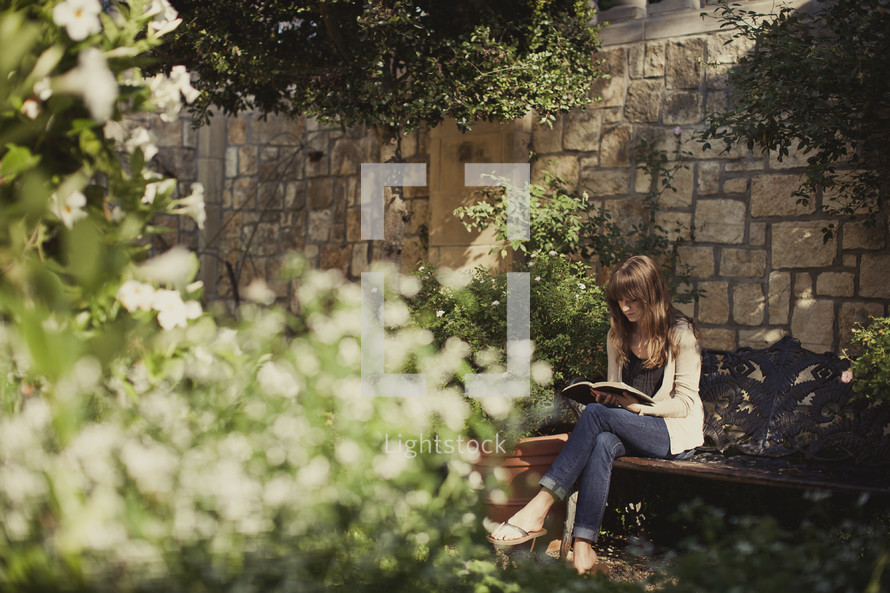 Woman reading bible on bench in garden,