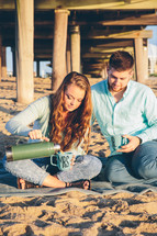 a couple having a picnic on a beach under a pier 