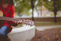 woman sitting outdoors playing a guitar 