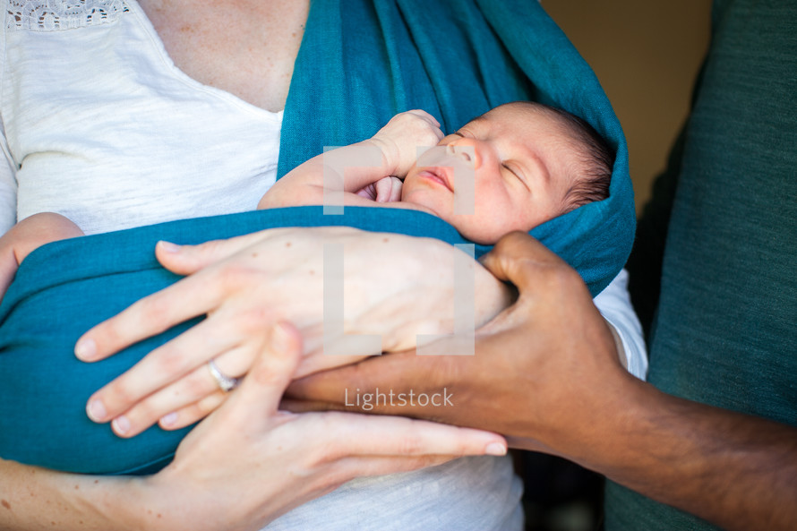 Parents' hands holding a newborn baby.